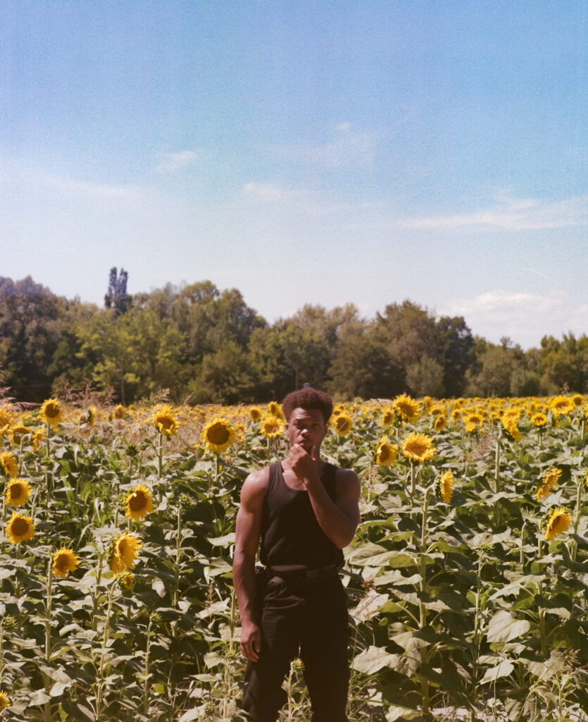Portrait d'un jeune homme vêtu de noir dans un champs de tournesol.