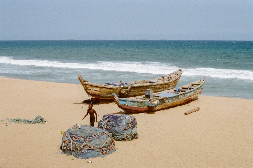 Photo avec deux barque sur la plage à Lomé et un enfant qui marche sur ma plage avec des filets de pêches